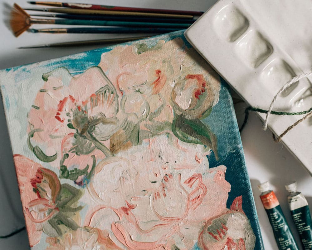 Colorful floral painting next to paintbrushes and paint palette